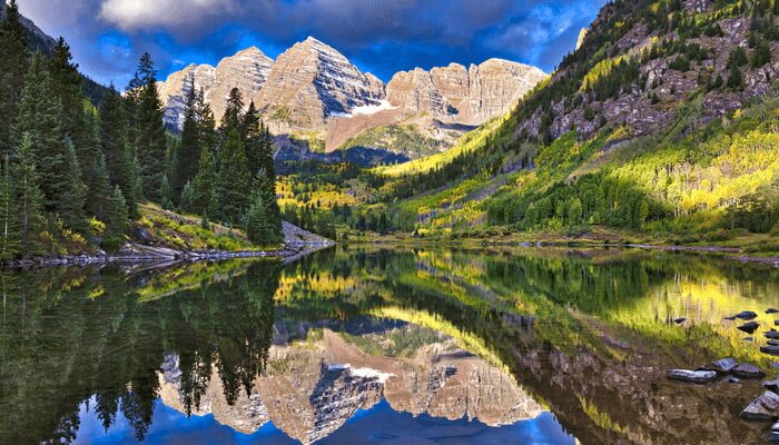 Image of the Maroon Bells in Aspen- with the iconic Maroon Bells reflected in Maroon Lake. The green wilderness and nature surrounds the area.