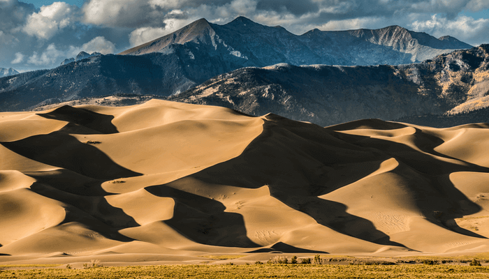 Image of the Great Sand Dunes National Park. There are mountains of sand with majestic views of mountains in the background.