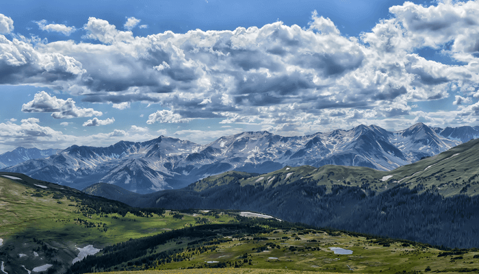 Image of Rocky Mountain National Park with views of the green grass, mountain range, and blue sky with clouds.