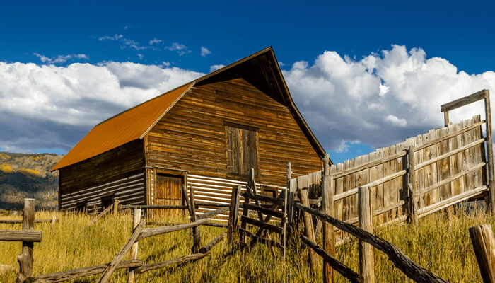 Image of a wooden cabin in Steamboat Springs, CO. In the background, the sky is blue with white clouds and there are yellow hills.
