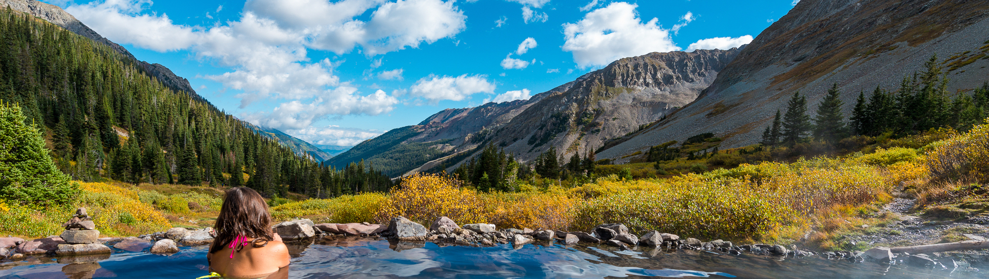 Image of a woman sitting in a natural hot spring in Colorado, soaking in the stunning mountain views from the pool