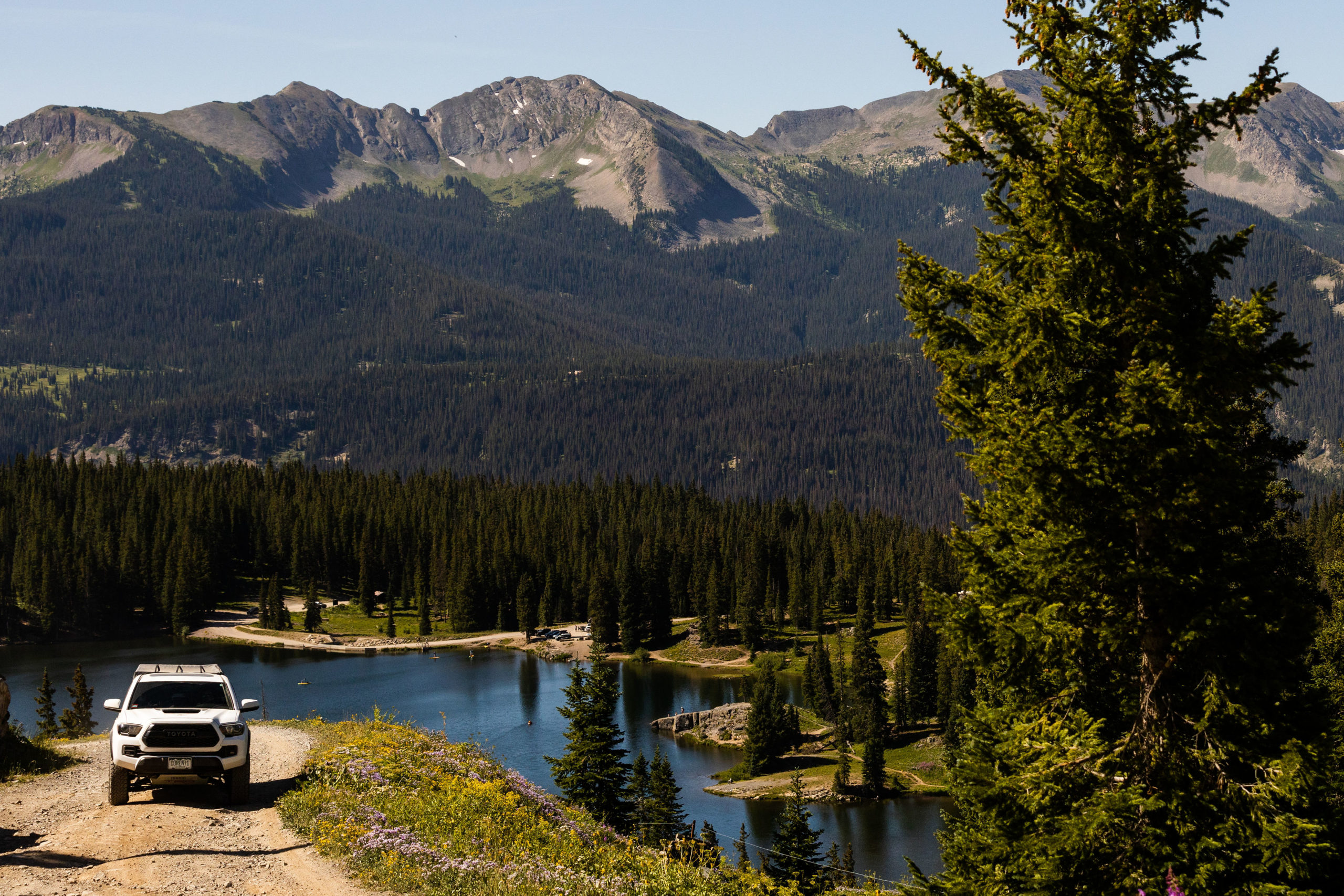 Image of a Colorado Overlander Tacoma driving up a dirt road with a serene lake in the background.