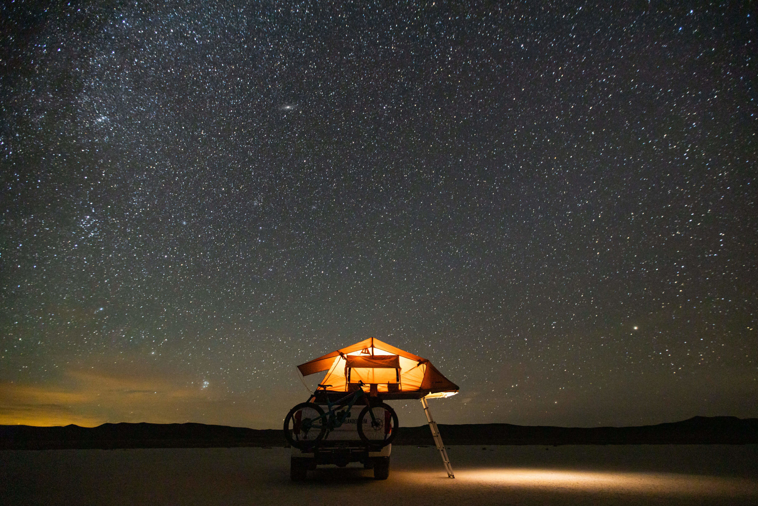 Image of a Colorado Overlander Toyota Tundra TRD Pro under a starry sky in the desert- the orange roof nest tent is lit up with a light