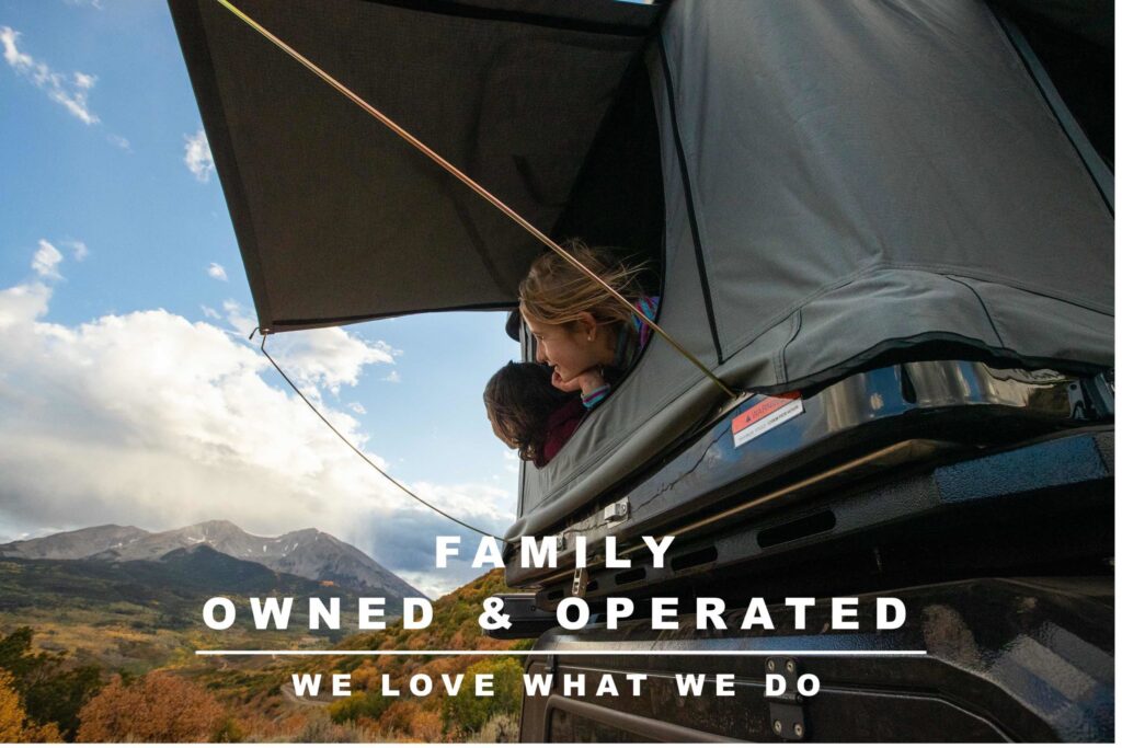 Image of two girls popping their heads out of the opening of a rooftop tent- they are looking towards the mountains and soaking in the fall beauty